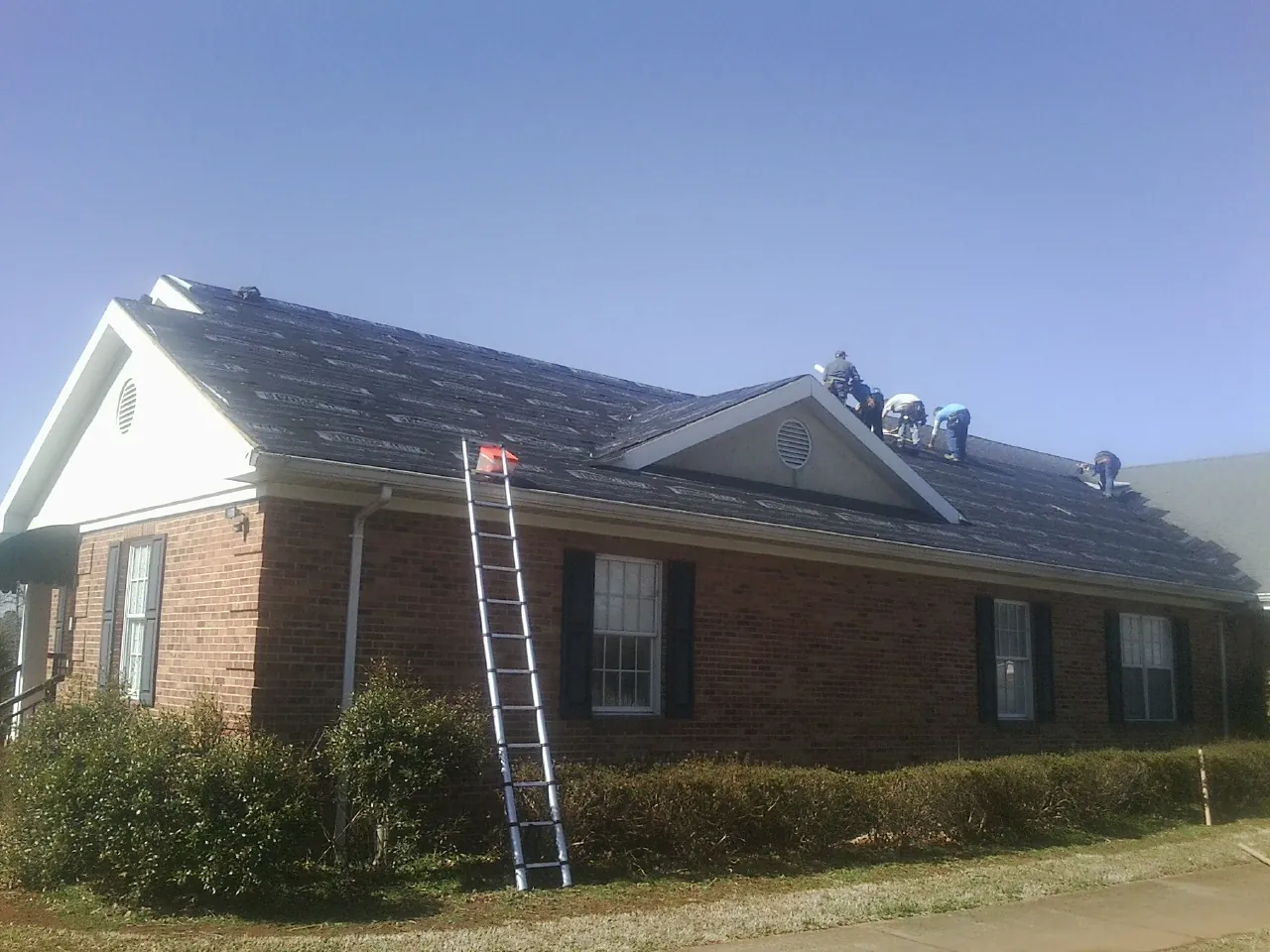 Crew tearing shingles off a brick ranch roof with a ladder set — Metal Roof Repair work by our crew in Mc Sherrystown
