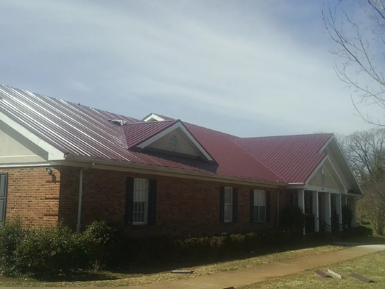 Red metal roof with gabled entries on a long brick building, from a Hail Damage Roof Repair job in Mc Sherrystown