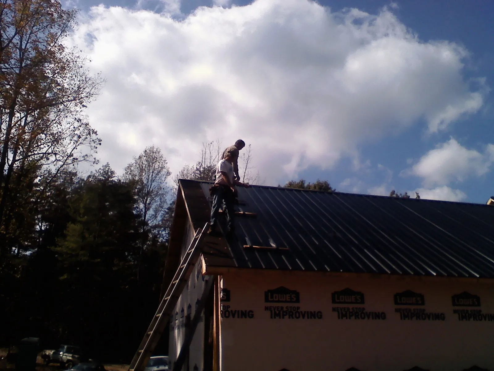 Roofer fastening dark metal panels high against a cloudy sky, from a Roof Inspection job in Mc Sherrystown