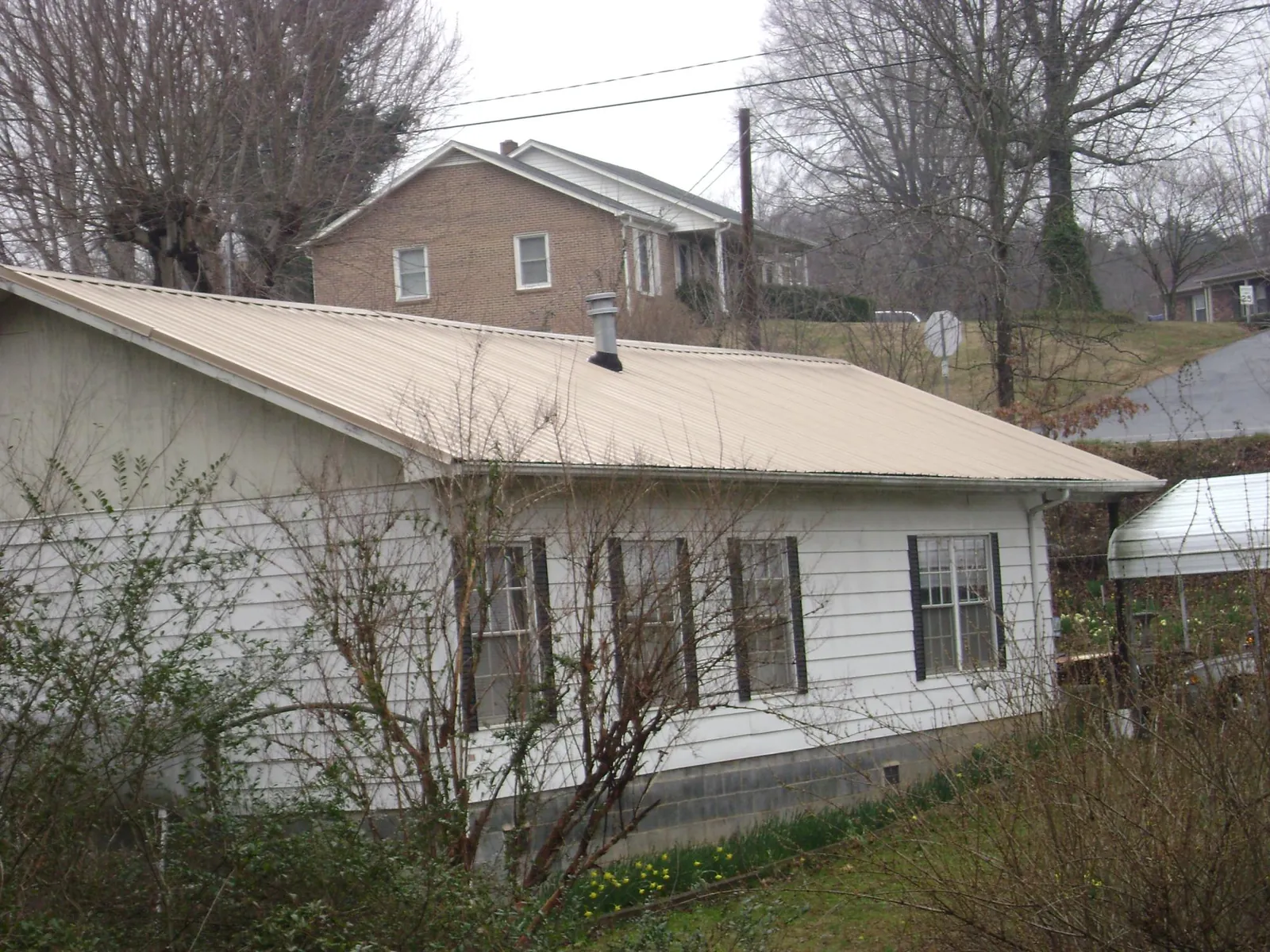 Tan metal roof on a white sided house set into a hillside — Commercial Roofing by Roofing Brothers in Mc Sherrystown